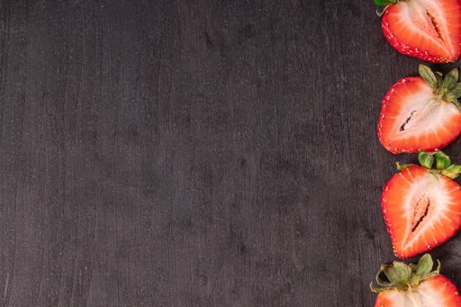 An overhead shot of strawberries cut in half on a dark wooden surface