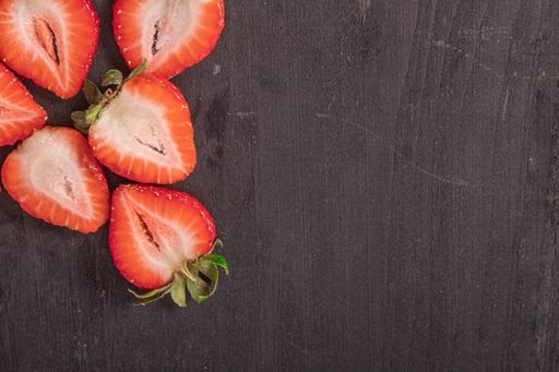 An overhead shot of strawberries cut in half on a dark wooden surface