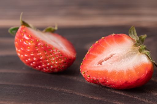 An overhead shot of strawberries cut in half on a dark wooden surface