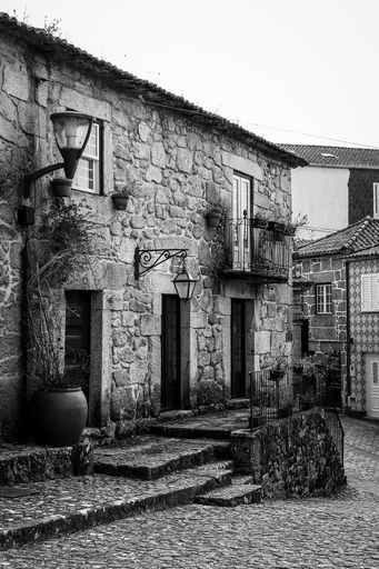 A vertical grayscale shot of a small brick building with lamps on its front wall in an old town