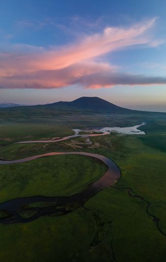 Panorama landscape wallpaper of green field, river and a mountain during the sunrise. Pink clouds over a green mountain and river. Aerial view.