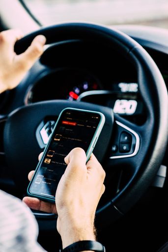 A vertical shot of a person texting on his phone while driving