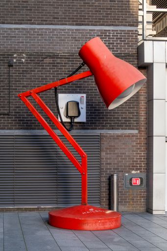 A red vintage-style lantern hanging on the wall of a brick building with its lampshade closed