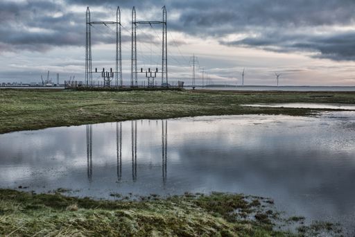 A low angle shot of a transmission line with a cloudy sky reflected on the water
