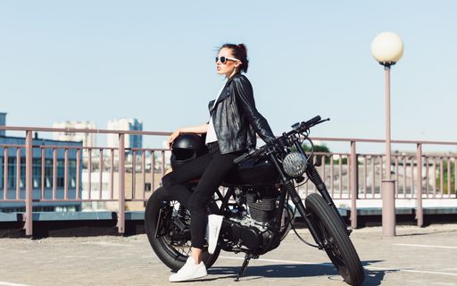 A young woman wearing a black leather jacket and trousers is posing with a motorbike