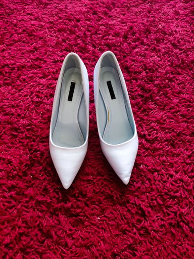 A vertical shot of a pair of white classic high heels on a fluffy pink rug