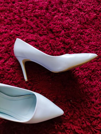 A vertical shot of a pair of white classic high heels on a fluffy red rug