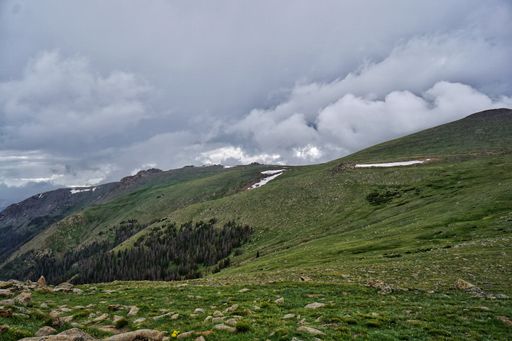 An idyllic alpine scene comprised of lush green grass, rocky terrain, and towering mountains in the background