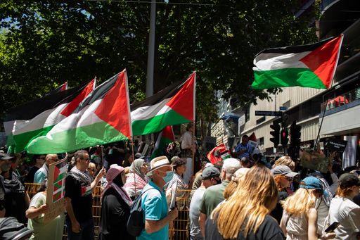 A diverse group of people marching together in solidarity, carrying brightly colored flags, stroll along a cobblestone road
