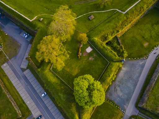 An overhead shot of a city park with green fields and a parking space