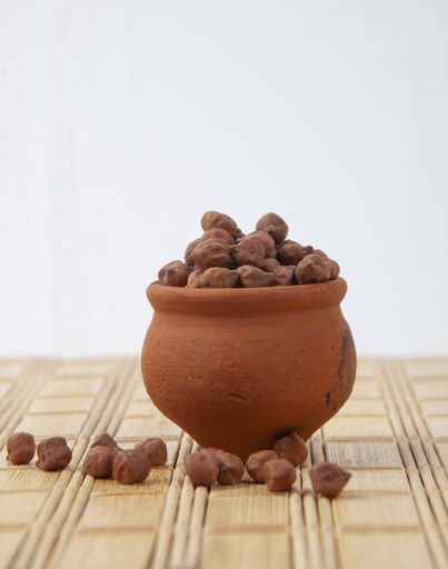 A vertical shot of ground nuts in a clay pot on a wooden mat against white wall background