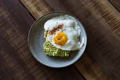 A top view of a healthy breakfast plate of fresh avocado toast with a fried egg on a wooden table