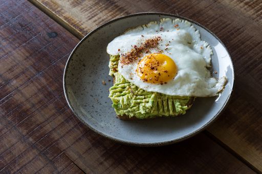 A healthy breakfast plate of fresh avocado toast with a fried egg on a wooden table