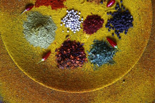 A top view of different condiments and small red chilies on a plate covered with yellow spice