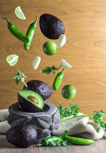 A vertical shot of healthy vegetables and fruits flying into the stone bowl put on a kitchen table