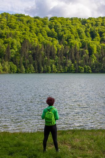 A beautiful shot of a female hiker in a green track jacket and a backpack admiring the mountain lake