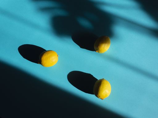 A top view of three fresh ripe lemons on a blue table under a bright sunlight