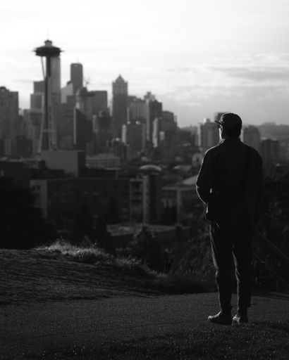 A man on a hillside, gazing out over a sprawling cityscape of Seattle, Washington, USA in grayscale