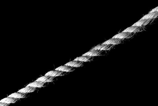 A greyscale closeup of a rope under the lights against a black background