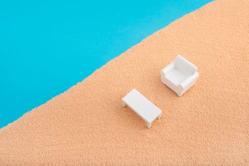 A miniature white armchair and table on the sand in contrast with blue background