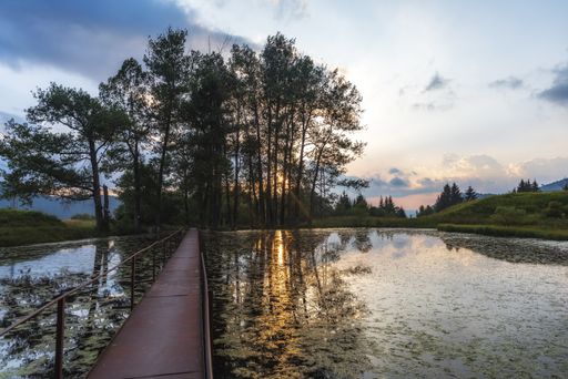 A high angle shot of a wooden bridge over the lake with the dramatic sky in the background