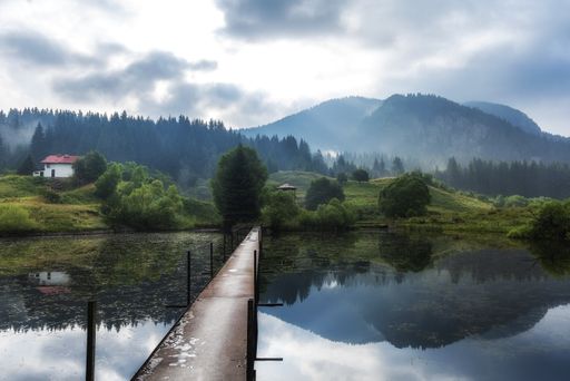 A high angle shot of a wooden bridge over the lake with the dramatic sky in the background