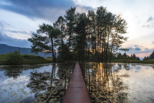A high angle shot of a wooden bridge over the lake with the dramatic sky in the background