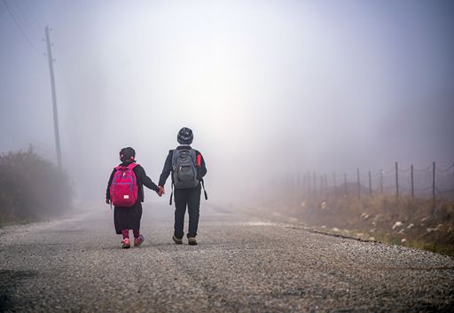 A back view of boy and girl pupils with school bags walking in the fog hand in hand