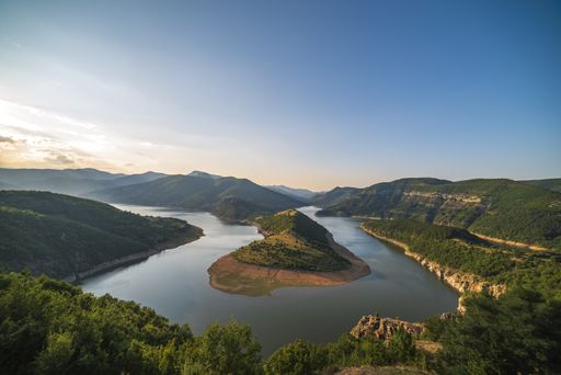 An aerial shot of the river flowing amount the mountains and hills during sunset