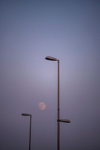 A vertical shot of street light poles and a full moon in the sky