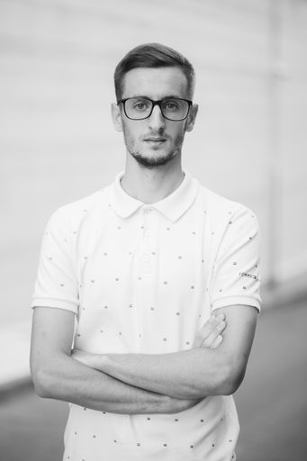 A grayscale shot of a handsome guy in glasses with his hands crossed