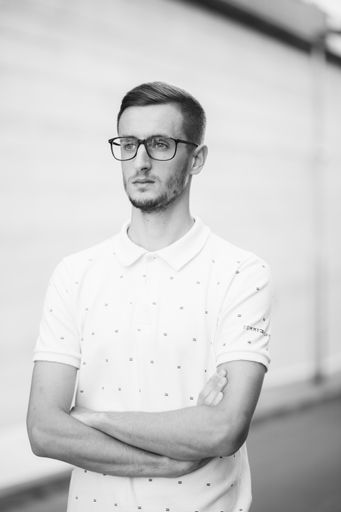 A grayscale shot of a handsome guy in glasses with his hands crossed