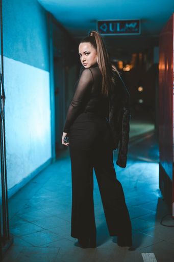 A shallow focus of an adult woman wearing a black sheer shirt with trousers under blue led lights outdoors