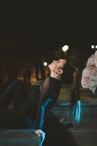 A shallow focus of a glamour woman wearing a black outfit and sitting on a wall in a park at night