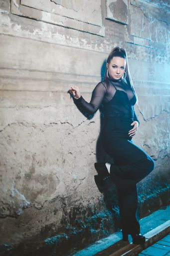 A vertical shot of a blonde Caucasian female posing in an elegant black robe leaning on a wall