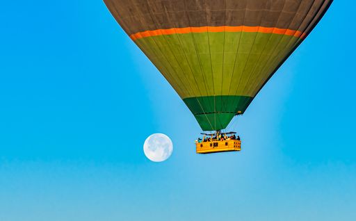 Colorful hot-air balloon flying over the Cappadocia region in Turkey in a blue sky with a full moon