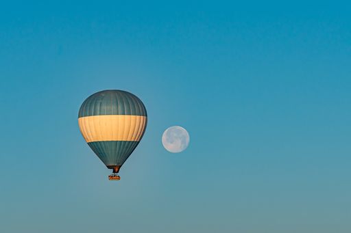 Colorful hot-air balloon flying over the Cappadocia region in Turkey in a blue sky with a full moon
