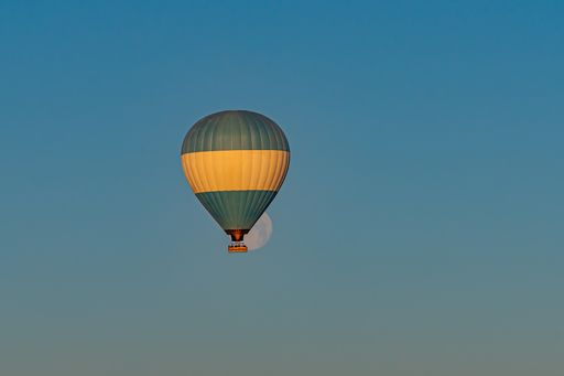 Colorful hot-air balloon flying over the Cappadocia region in Turkey in a blue sky with a full moon