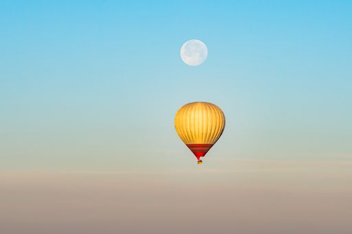 Colorful hot-air balloon flying over the Cappadocia region in Turkey in a blue sky with a full moon