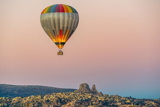 Colorful hot-air balloon flying over the Cappadocia region and Uchisar castle in Turkey in an orangsky
