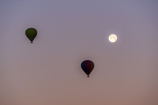 The silhouette of hot-air balloons flying over the Cappadocia in Turkey in a pink sky with a full moon