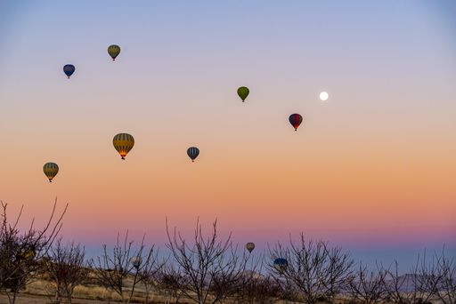 Colorful hot-air balloons flying over the Cappadocia in Turkey in an orange and blue sky with a full moon