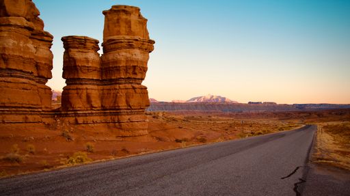 A solitary motorcyclist is travelling along a deserted desert road, surrounded by majestic rock formations in the backdrop