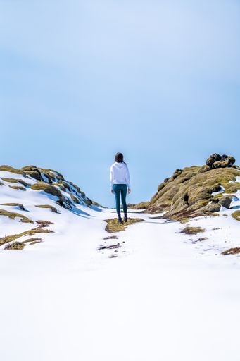 A person stands silhouetted against a snow-covered hill, their back facing the camera