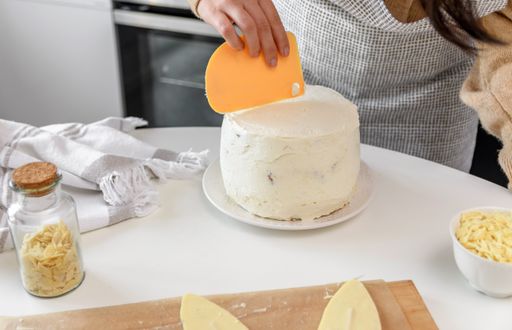 Close-up image of woman baking and decorating cake. Woman using spatula to apply white icing or frosting on a cake.