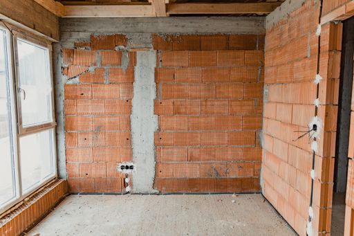 an indoor construction site with a big window, brown bricks and concrete ground