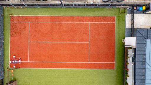 an aerial view of a red-green tennis court with black fences