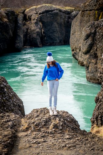 A young woman stands atop a rocky outcropping, gazing out at the majestic mountain stream below her