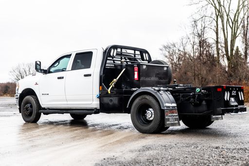 A white pickup truck with a flatbed trailer attached is pictured, with a bright blue sky in the background