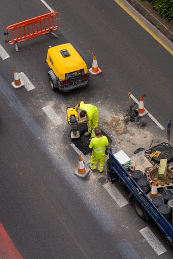Vertical photo of construction workers repairing the sewer in the street. View from above.